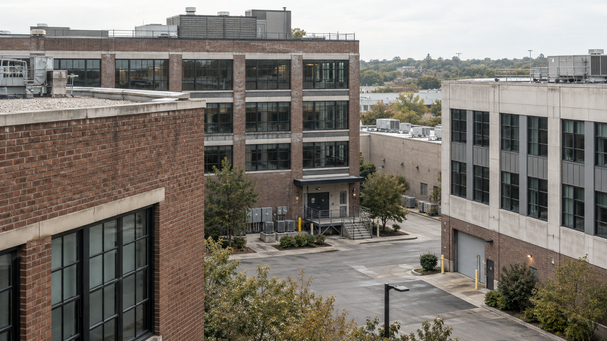 A foreground brick building partially frames several neighboring properties and a service courtyard.